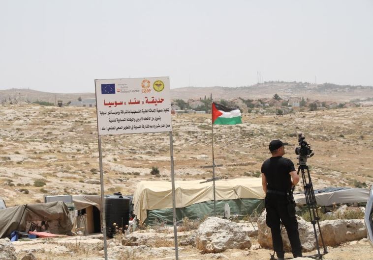 The tents of the illegal Palestinian village of Sussiya, with the Jewish settlement in the background. An EU logo is on a sign not far from the Palestinian flag