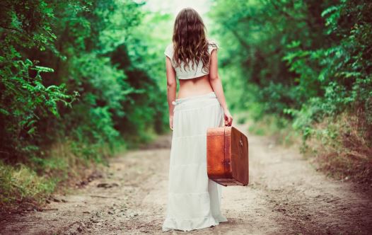 Young woman with suitcase in hand going away by a rural road