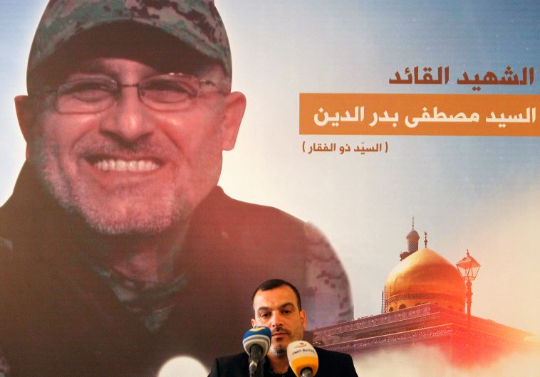 A man reads the Koran in front of a picture depicting top Hezbollah commander Mustafa Badreddine