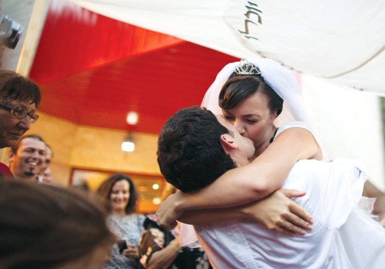 A bride and groom kiss under the chuppah at their wedding