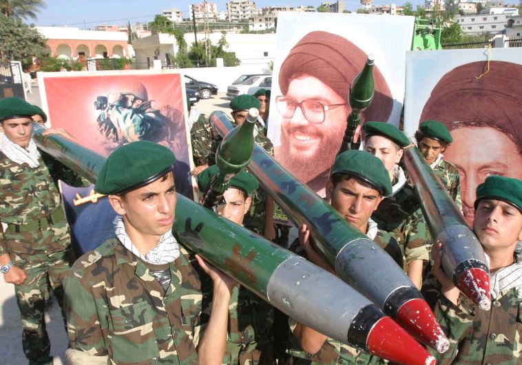 Hezbollah members carry mock rockets next to a poster of the group's leader Sayyed Hassan Nasrallah [FIle]